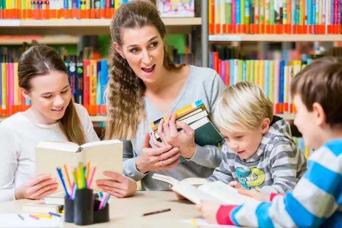 Eine Frau liest mehreren Kindern in einer Bibliothek aus einem Buch vor, Symbolbild zum Vorlesetag